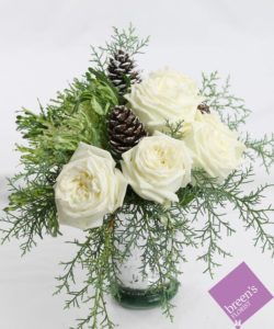 this arrangement features 1/2 dozen white roses accented with Christmas greens, pine cones, and ornamental kale in a mercury glass vase.