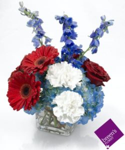 Blue hydrangea, blue delphinium with red and white blooms in cube vase