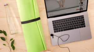 Green yoga mat on wood floor, water bottle, and virtual yoga class on laptop